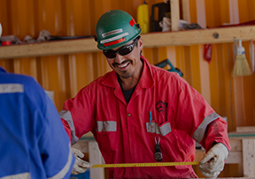 Man in sunglasses and orange coverall holding measuring tape