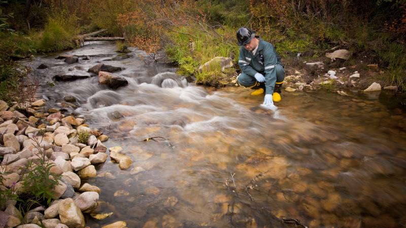 Person crouched beside river taking water samples