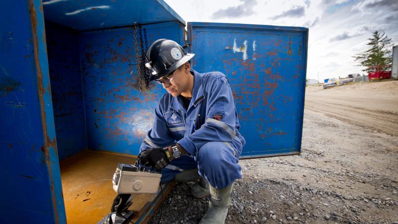 Person in hardhat crouched beside blue box